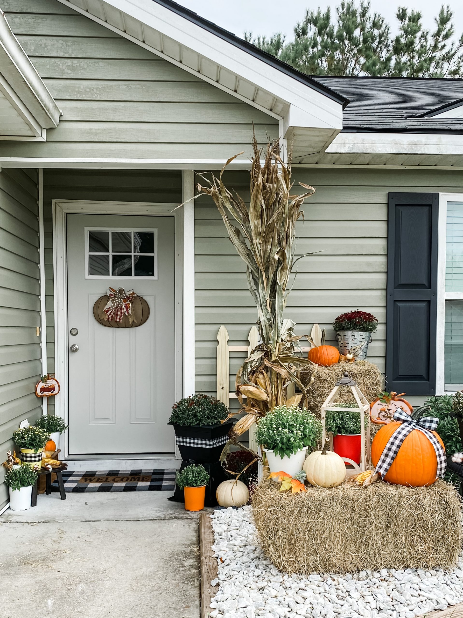 Finished fall front porch decorated with layered pumpkins, colorful mums, hay bales and cornstalks