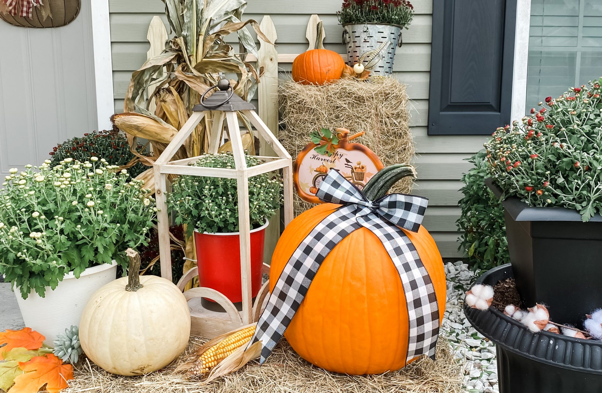 Orange and white pumpkins layered with a fall mum, wooden lantern and buffalo check ribbon