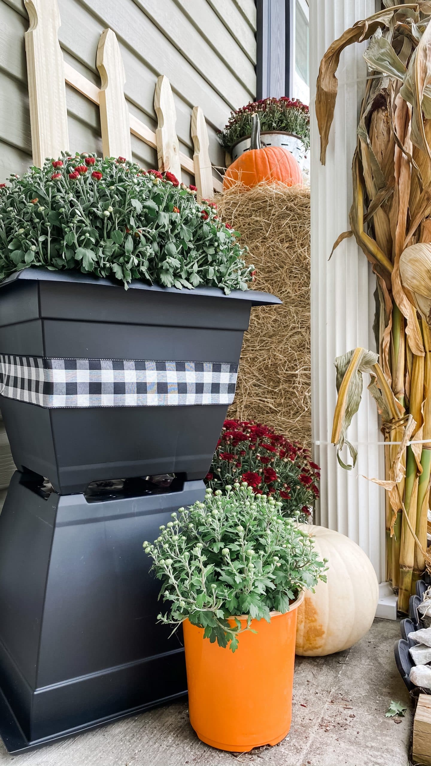 Colorful fall mums displayed at different heights in stacked black planters beside the front door