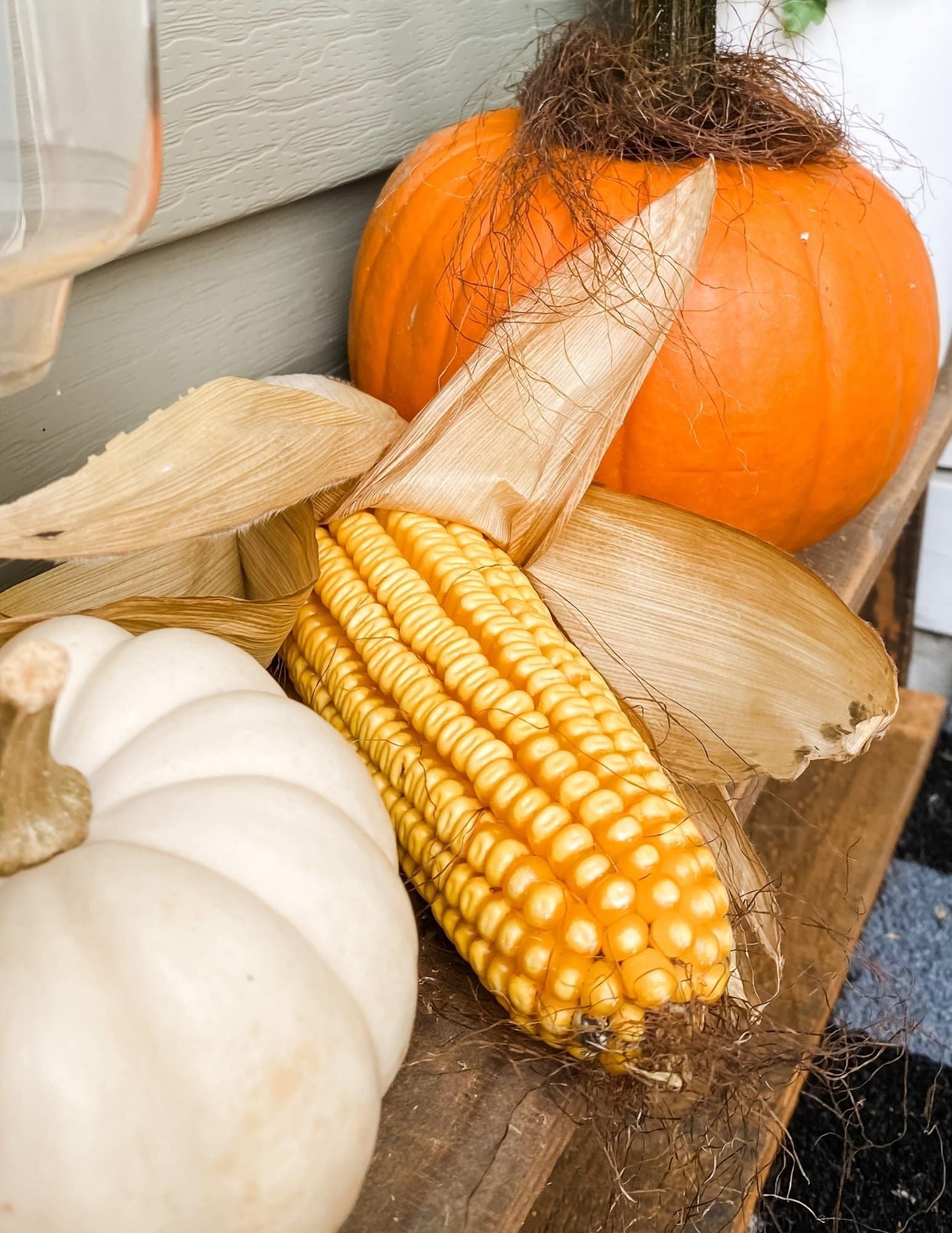 Corn and small pumpkins tucked between decorations on the fall front porch