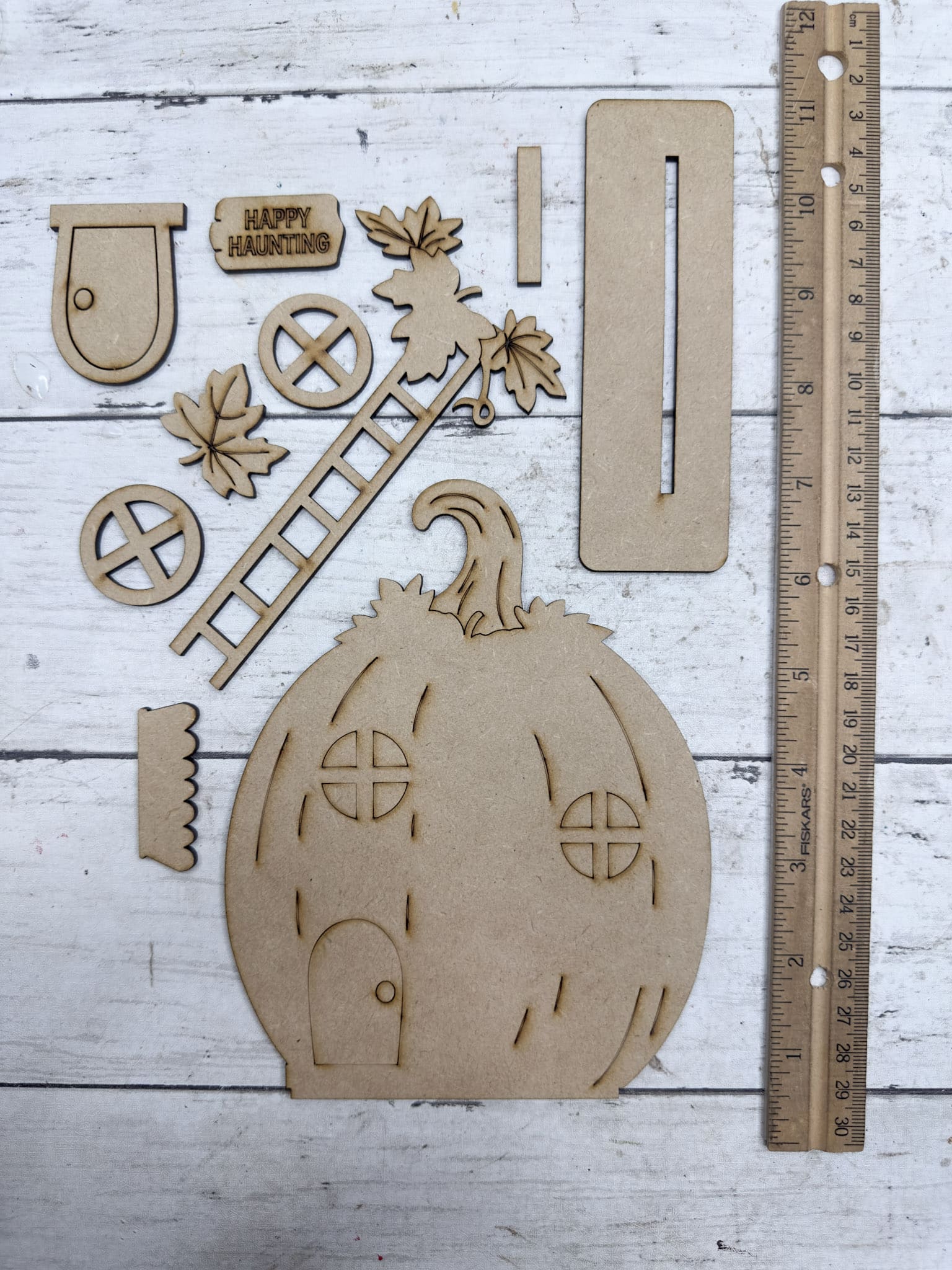 Happy Haunting Pumpkin House DIY kit pieces laid out unfinished with pumpkin base, windows, ladder, leaves, door, sign and stand.