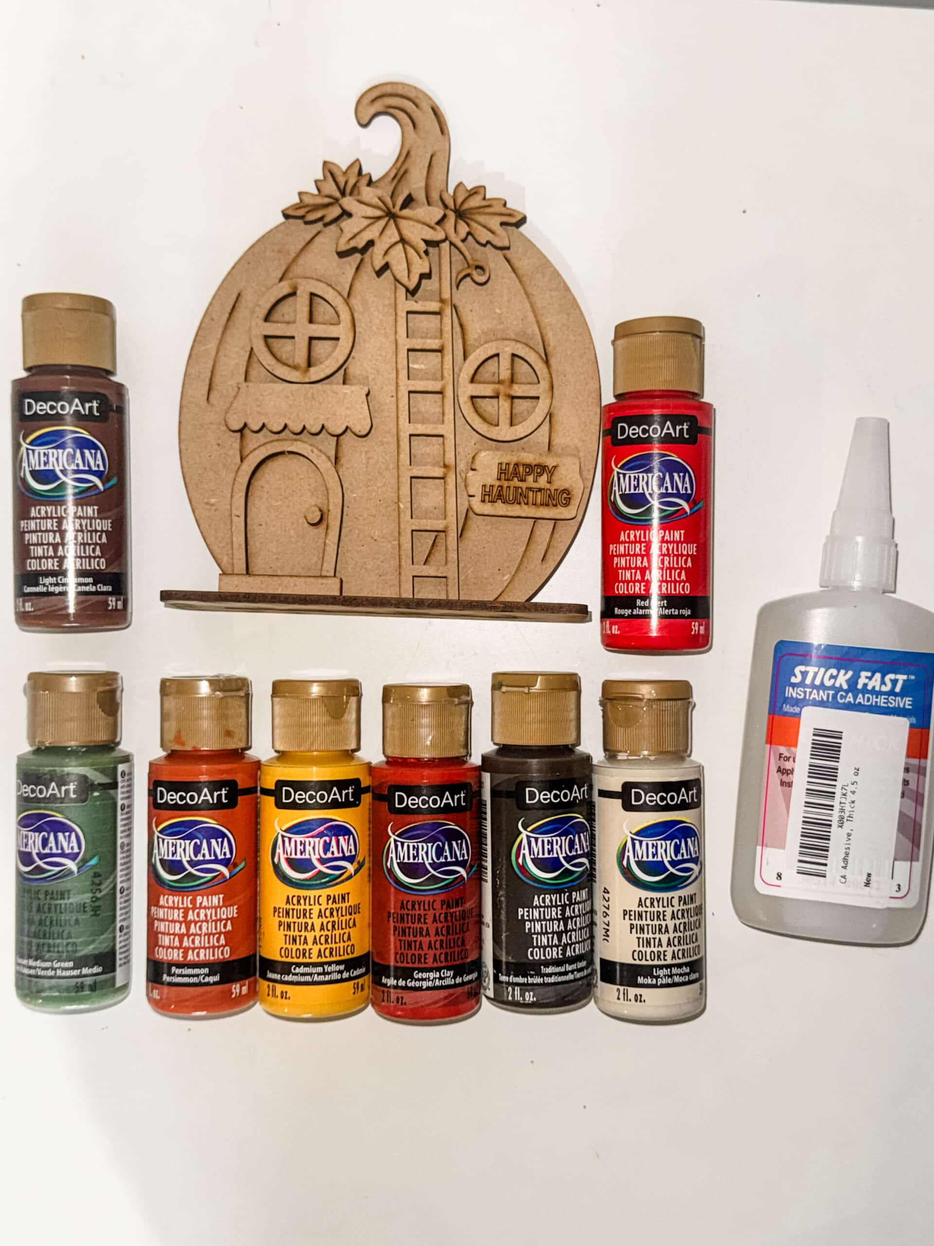 Happy Haunting Pumpkin House DIY craft kit with acrylic paint colors and adhesive used to create the finished fall and Halloween pumpkin house.