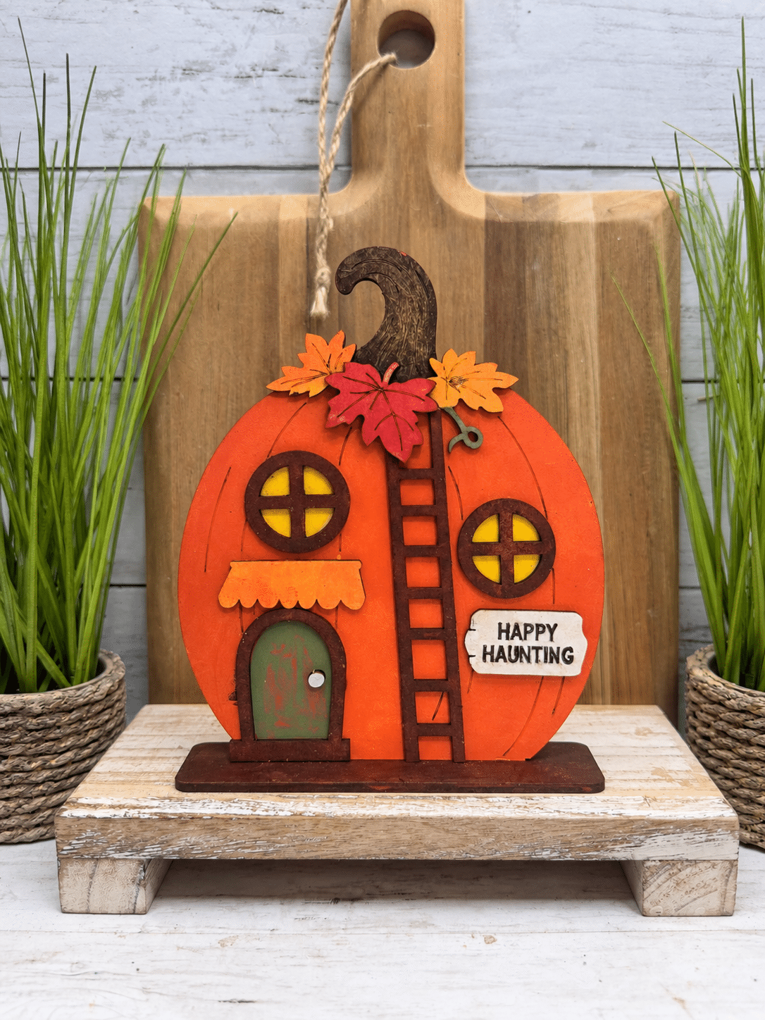 Finished Happy Haunting Pumpkin House DIY craft kit painted orange and staged with rustic wood decor and greenery for fall and Halloween.